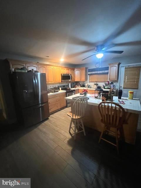 kitchen with appliances with stainless steel finishes, tasteful backsplash, a breakfast bar area, ceiling fan, and light wood-type flooring