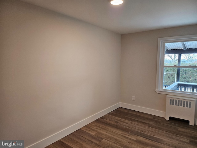 empty room with dark hardwood / wood-style flooring and radiator heating unit