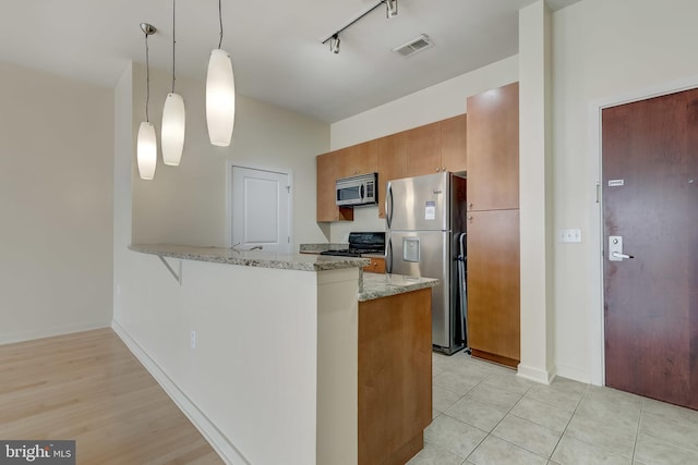 kitchen featuring kitchen peninsula, appliances with stainless steel finishes, rail lighting, light stone countertops, and pendant lighting