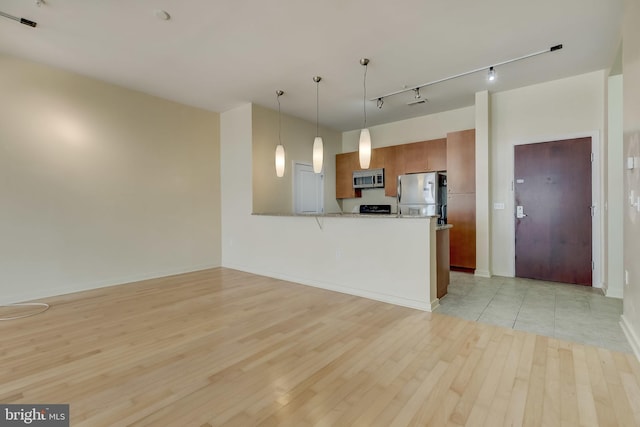 kitchen with kitchen peninsula, appliances with stainless steel finishes, a breakfast bar, light hardwood / wood-style flooring, and hanging light fixtures