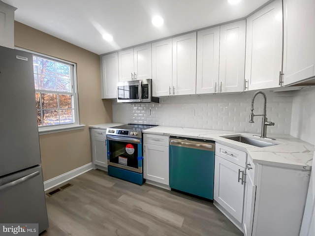 kitchen with light stone countertops, white cabinetry, stainless steel appliances, sink, and backsplash