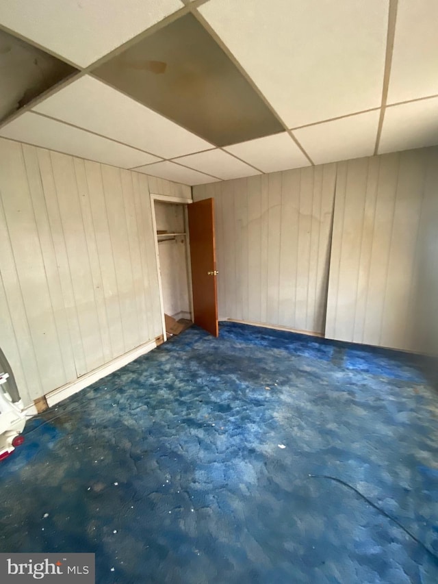 basement featuring a paneled ceiling and wood walls