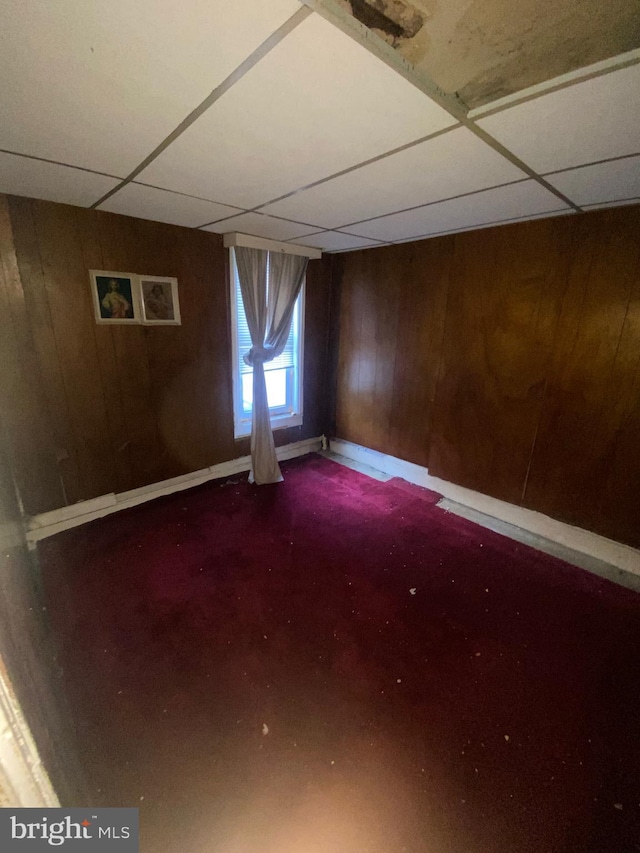 basement with a drop ceiling and wooden walls