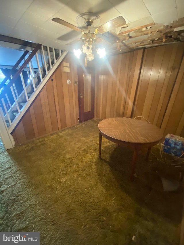 living area featuring carpet, ceiling fan, and wooden walls