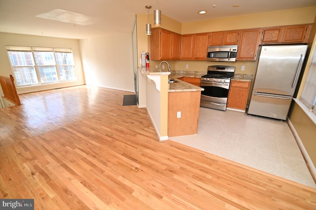 kitchen featuring a breakfast bar, decorative light fixtures, light hardwood / wood-style floors, kitchen peninsula, and stainless steel appliances