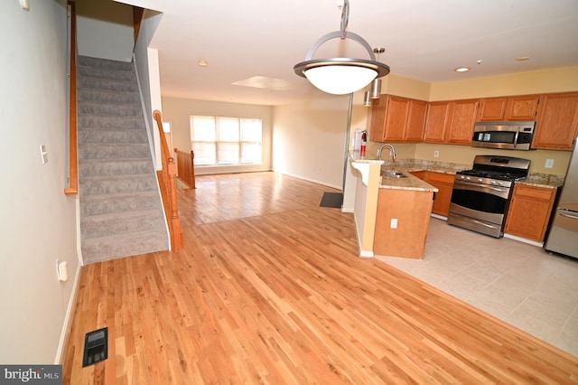 kitchen with stainless steel appliances, light stone counters, light hardwood / wood-style floors, and sink