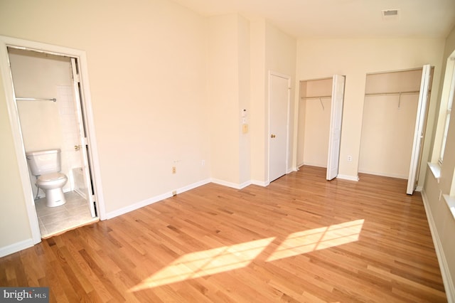 unfurnished bedroom with connected bathroom, two closets, light hardwood / wood-style flooring, and vaulted ceiling