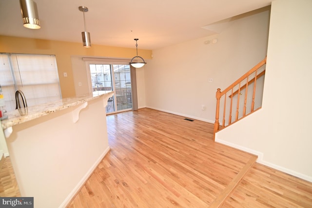 kitchen featuring light stone counters, a breakfast bar, hanging light fixtures, and light hardwood / wood-style floors