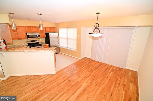 kitchen featuring decorative light fixtures, kitchen peninsula, stainless steel appliances, and light hardwood / wood-style flooring