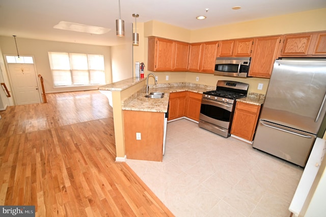 kitchen featuring kitchen peninsula, appliances with stainless steel finishes, a kitchen bar, light stone countertops, and pendant lighting