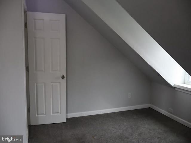 bonus room with dark colored carpet and vaulted ceiling with skylight