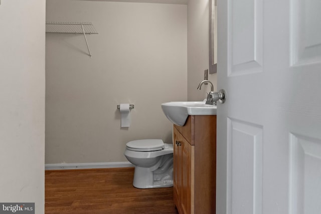 half bathroom featuring toilet, baseboards, wood finished floors, and vanity