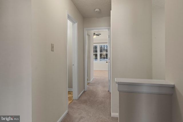 hallway with carpet, baseboards, and a textured ceiling