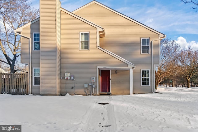 snow covered house featuring a chimney and fence