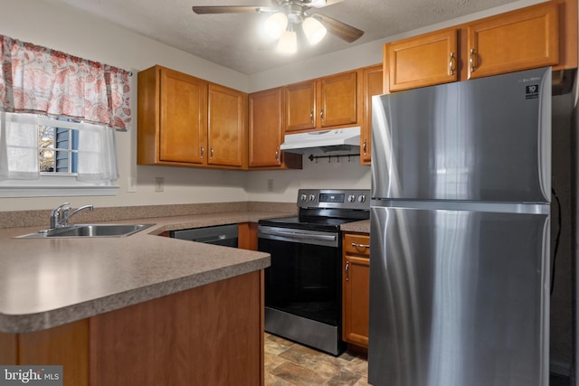 kitchen featuring brown cabinets, stone finish flooring, stainless steel appliances, under cabinet range hood, and a sink