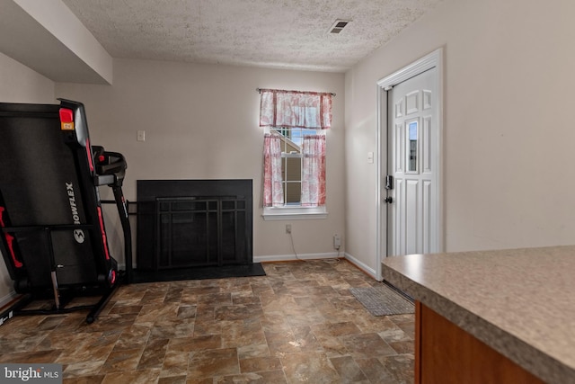 foyer entrance featuring baseboards, visible vents, stone finish flooring, a textured ceiling, and a fireplace