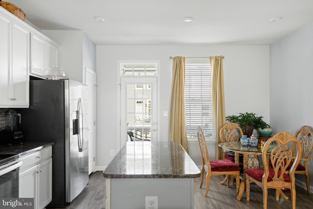 kitchen featuring dark hardwood / wood-style flooring, dark stone counters, stainless steel appliances, white cabinets, and a center island