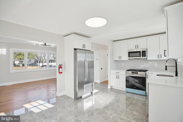 kitchen featuring decorative backsplash, appliances with stainless steel finishes, sink, a notable chandelier, and white cabinetry