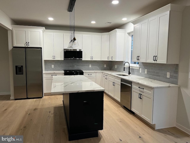 kitchen with appliances with stainless steel finishes, a kitchen island, sink, pendant lighting, and white cabinetry