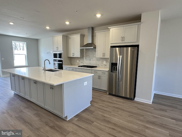 kitchen featuring white cabinetry, wall chimney range hood, gas cooktop, stainless steel fridge, and an island with sink