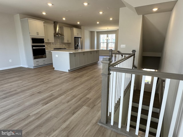 kitchen featuring backsplash, a center island with sink, stainless steel refrigerator with ice dispenser, wall oven, and white cabinetry