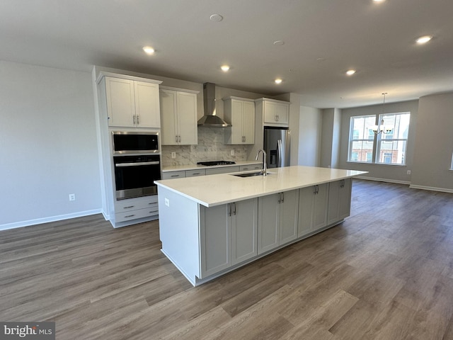 kitchen featuring white cabinetry, an island with sink, wall chimney exhaust hood, and stainless steel appliances