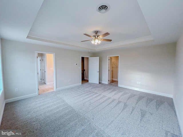 unfurnished bedroom with a tray ceiling, a walk in closet, ceiling fan, and carpet