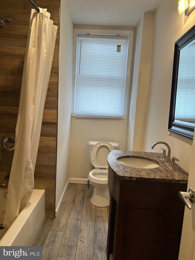 bathroom featuring toilet, shower / bath combo, vanity, wood finished floors, and baseboards