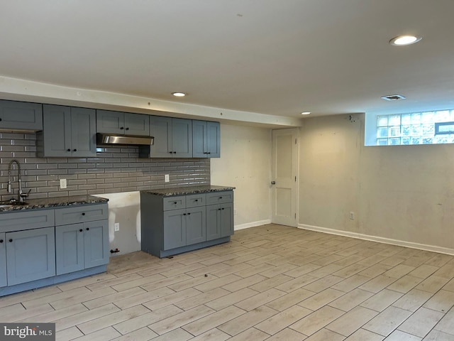 kitchen featuring tasteful backsplash, a sink, dark stone countertops, under cabinet range hood, and baseboards