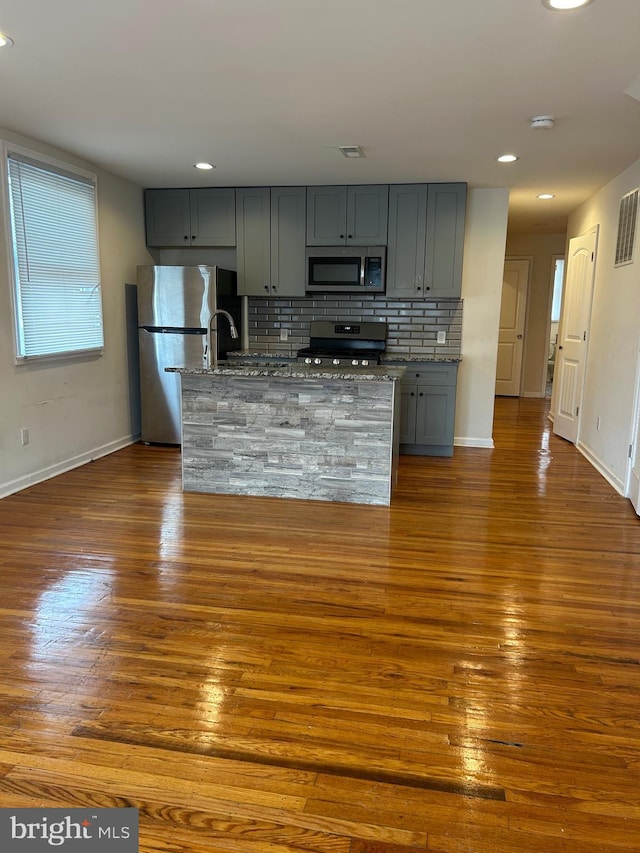 kitchen with appliances with stainless steel finishes, dark wood finished floors, backsplash, and gray cabinetry