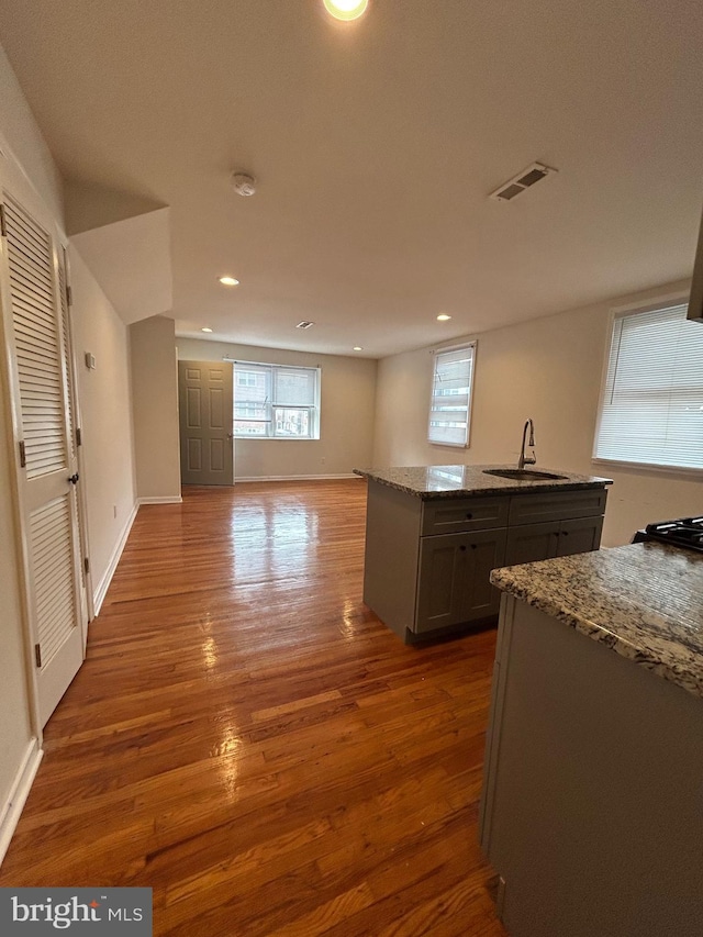 kitchen with a kitchen island with sink, visible vents, a sink, and light stone countertops