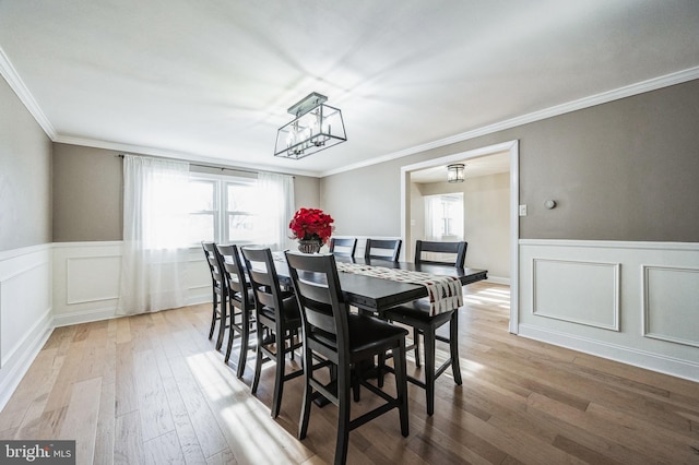 dining area with ornamental molding, light wood-type flooring, and an inviting chandelier