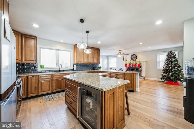 kitchen with ceiling fan, a center island, beverage cooler, pendant lighting, and light hardwood / wood-style floors