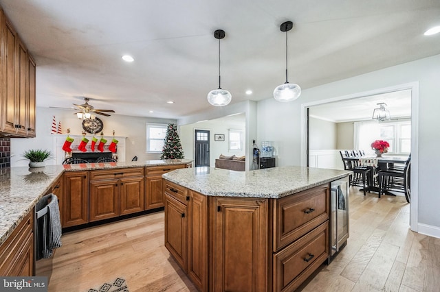 kitchen with pendant lighting, light hardwood / wood-style floors, light stone countertops, and beverage cooler