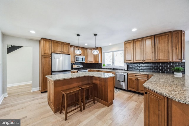 kitchen with light stone countertops, appliances with stainless steel finishes, sink, light hardwood / wood-style flooring, and a center island