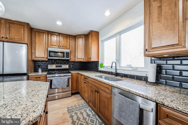 kitchen featuring sink, light hardwood / wood-style flooring, decorative backsplash, light stone counters, and stainless steel appliances