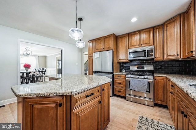 kitchen with light stone countertops, hanging light fixtures, stainless steel appliances, decorative backsplash, and a kitchen island