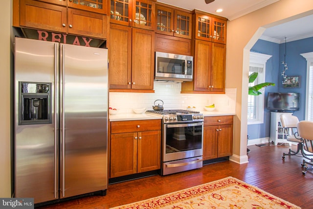 kitchen featuring hanging light fixtures, ornamental molding, tasteful backsplash, dark hardwood / wood-style flooring, and stainless steel appliances