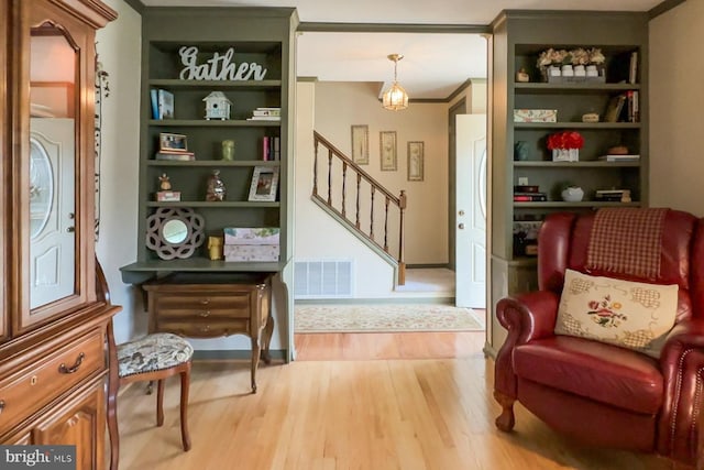 sitting room featuring built in shelves, crown molding, and light hardwood / wood-style flooring