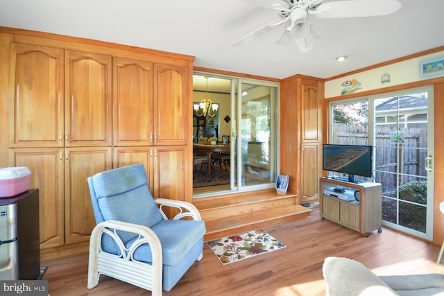 living area with ceiling fan with notable chandelier, crown molding, and light hardwood / wood-style floors