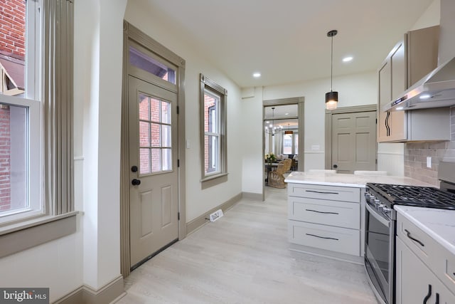 kitchen with backsplash, wall chimney exhaust hood, light wood-type flooring, decorative light fixtures, and gas stove