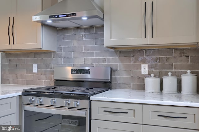 kitchen featuring tasteful backsplash, light stone counters, wall chimney exhaust hood, white cabinets, and stainless steel range with gas cooktop