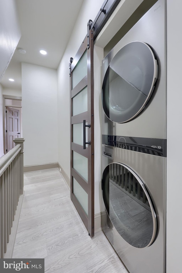 laundry area with stacked washer / dryer, light hardwood / wood-style flooring, and a barn door