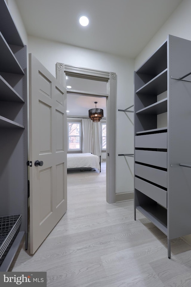 walk in closet with light wood-type flooring and an inviting chandelier