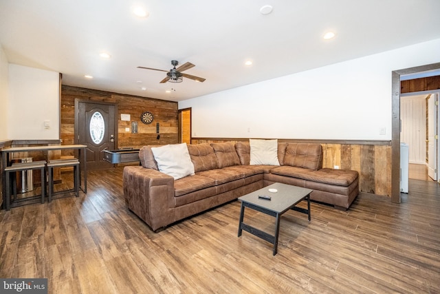 living room featuring hardwood / wood-style flooring, ceiling fan, and wooden walls