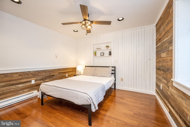 bedroom featuring ceiling fan, wooden walls, and a baseboard radiator