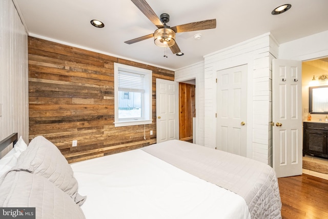 bedroom with wooden walls, ceiling fan, ensuite bathroom, and hardwood / wood-style flooring