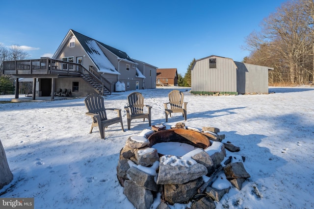 yard covered in snow with a wooden deck, an outbuilding, and a fire pit