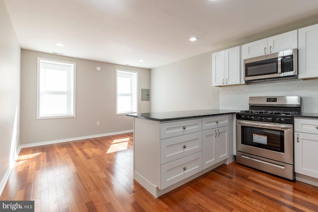 kitchen with tasteful backsplash, kitchen peninsula, hardwood / wood-style flooring, appliances with stainless steel finishes, and white cabinets