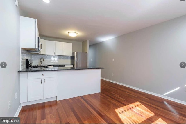 kitchen with white cabinets, dark hardwood / wood-style flooring, dark stone counters, decorative backsplash, and stainless steel refrigerator